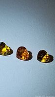 Three heart-shaped natural sapphire gemstones arranged side by side on a flat surface, with visible facets and bright yellow to orange coloration.