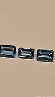 Three rectangular emerald cut Swiss blue topaz gemstones shown on a neutral background highlighting their deep blue color and clarity