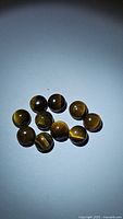 Ten natural round cabochon yellow tiger's eye gemstones with golden to brown chatoyancy against a white background.