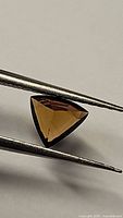 Front view of natural trillion cut deep yellow tourmaline held by tweezers showing color and cut details.