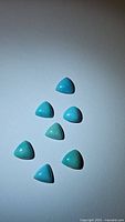 Seven natural turquoise stones with smooth trillion cabochon cuts, arranged on white background, showing color variations in robin's egg blue tones.