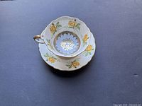 Top-down photo of the cup inside the saucer showing the yellow rose floral pattern, light blue inner circle with gold floral details, and gold trim edges.