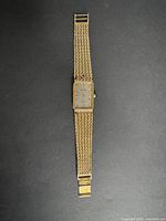 Full view of vintage gold plated Bulova men's watch with rectangular face and mesh bracelet laid flat.