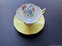Top view of vintage porcelain bone china Hammersley cup placed on matching yellow saucer with floral patterns on the inside of the cup and gold trim on rims.