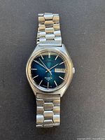 Front view showing entire watch face and bracelet with day-date display and blue gradient dial.