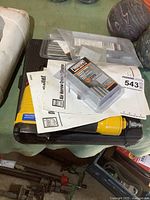 Yellow air nailer, carrying case, manuals, and packs of nails and staples on a table