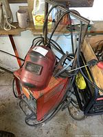 Full view of the Canox arc welder on custom cart with welding helmet resting on top and cables wrapped around the cart handles.
