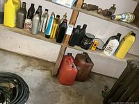 Photo of two shelves holding various plastic and metal bottles of automotive lubricants and fluids, and two red fuel cans on the floor.