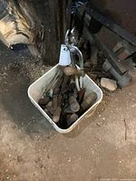 Bucket filled with multiple old copper soldering irons, blacksmithing tools and a copper hammer, all showing aged wear.