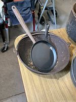 Cast iron cauldron with handle, small frying pan placed inside, and ladle resting on cauldron