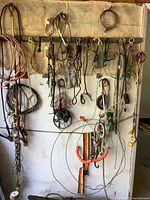 Wall-mounted assortment of metal chains, cables, hooks, pulleys, and cables, showing full lot from a front view.