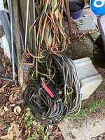 Bundles of assorted older copper wires and thick welder cables resting on cinder blocks and metal frame outdoors with dry leaves nearby.