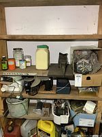 Three shelves filled with various electrical parts, containers, motors, and mechanical items in unorganized arrangement.
