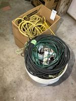 Photo showing a large cardboard box filled with thick yellow rope and a white bucket containing coil of black and green electrical wires with some electrical components inside.