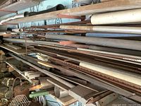 Wide view of the shelving rack filled with assorted long steel rods, pipes, angle irons, and flat bars showing various surface conditions and sizes