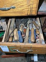 Open wooden drawer containing a collection of hand files with wooden and blue plastic handles, showing wear and use.