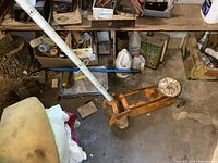 Orange heavy duty floor jack with white handle and wheels, placed on concrete floor with other items in background.