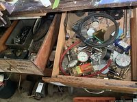 View of two wooden drawers containing assorted gauges, hoses, gears, coupler, and various small mechanical parts.