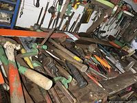 Bench-top and shelf with an assortment of hand tools including pipe wrenches, hammers, punches, and squares laid on a wooden surface.