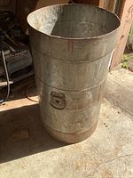 Heavy duty galvanized steel trash can with side handles, showing exterior surface, rust, and wear.