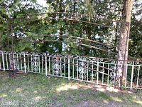 Front view of the large steel arbour showing the full width with decorative white and brown painted metal scrollwork panels and arch top.