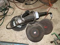 Angle grinder with handle and multiple abrasive discs on concrete floor