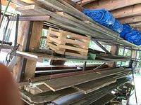 Side view of wooden planks and metal pipes on inside rack with blue tarp rolled on top.