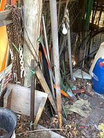 Photo showing assorted metal rods leaning against a wooden post, metal chains hanging, angle iron, tubing and a blue and white plastic container in the shed.