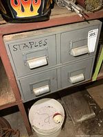 Front view of one metal 2-drawer cabinet marked 'STAPLES' on the top left drawer, showing contents and condition