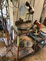 Full view of Delta 10-inch bench top miter saw on metal stand with spare blades and wheels.