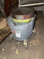 Overall view of vintage metal mop bucket with two smaller metal pails stacked inside, showing the items' condition and wear.