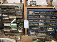 Two organizers side by side, one metal with labels and another blue plastic with clear drawers, both containing assorted hardware items.
