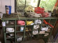 Wide shot showing green metal cabinet filled with assorted plumbing pipes, fittings, chains, and hardware components including boxes and bags.