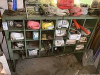 Full view of green wooden parts cabinet filled partially with various mechanical parts and containers.