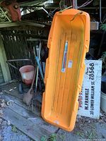 Photo taken showing the orange sled upright, displaying length and minor wear on the surface