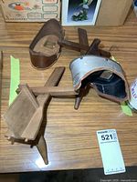 Two antique stereoscope viewers on a wooden table, one complete with metal and leather hood and wooden handle, the other incomplete wooden frame.