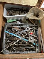 Overhead shot of metal trays containing various used taps, dies, and threading tools, with some saw blades and metal rods visible.