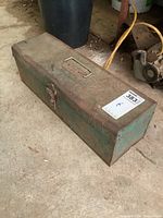Closed rusty green metal toolbox with handle on top and latch closure, showing age wear and surface rust.