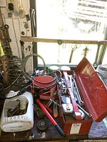 Photo of open red metal toolbox on a workbench showing hand tools including wrenches, hammer, tapes, bits, cable and fittings inside.