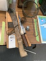 Overview of items showing machete, carving knives, frying basket, egg retriever, and thimble on a wooden surface