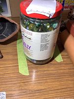 A 6 inch tall vintage glass jar filled with assorted vintage glass marbles. The jar has a red lid and retail grape jelly label from President's Choice.