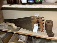 Three vintage wood-handled handsaws and two cast iron weights on a shelf with a label