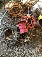 Multiple coiled lengths of copper wire in various colors and gauges, including a partial spool of pink insulated wire. Visible dirt and wear on wires. Ground surface visible with debris.