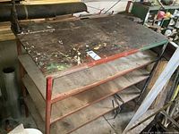 Front side view of metal framed workbench with pipe clamp vise and wooden shelves, showing work surface wear.