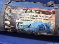 Photo of the blue carry bag with product label showing the tent details including brand, size, features, and a tent image.