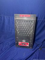 Front view of the coin operated Plinko style game machine showing black metal peg board, clear plastic cover, and bright red 25¢ coin label.
