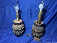 Two wagon wheel center post lamps with bulbs, cords and harp frames against a blue backdrop.