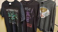Three rock and roll shirts hanging side by side showing front graphics.
