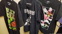 Three black graphic T-shirts laid side by side: Jelly Roll, Stevie Ray Vaughan, Street Fighter