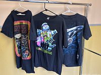 Three black T-shirts on hangers with TV show graphics: Stranger Things, Ghostbusters, Star Trek.
